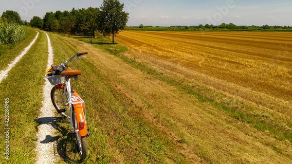 Obraz Summer landscape of the Venetian plain. Orange bicycle on the dirt road near a wheat field after harvest. Warm sunny day.