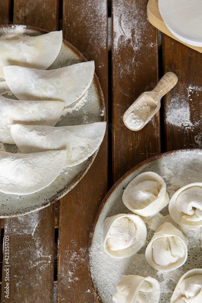 Fototapeta Raw homemade dumplings on two plates on a dark wooden table.