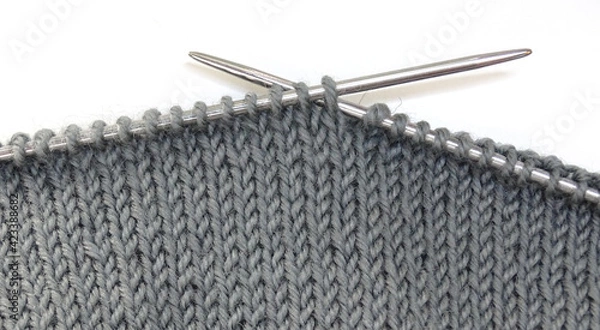 Fototapeta Knitting on knitting needles. Gray woolen fabric on knitting needles on a white background