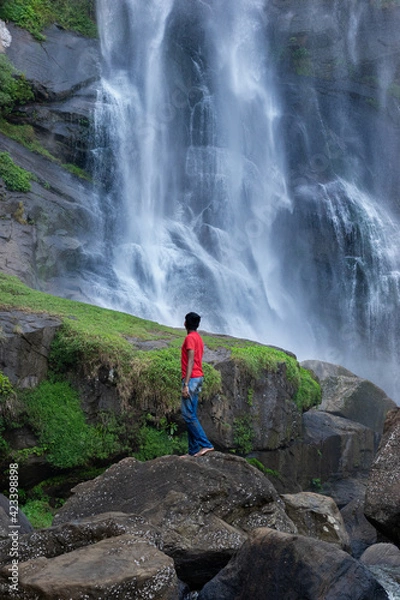 Obraz A boy standing next to a waterfall