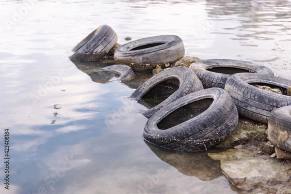 Fototapeta Old tires on the beach. Pollution of the reservoir with old car tires. Garbage on the shore