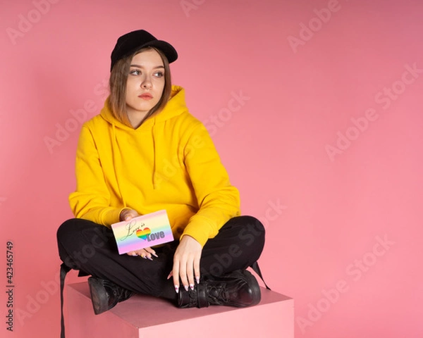 Fototapeta Girl sits on a pink cube and holds a card with the words love is love and lgbt heart
