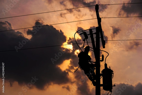 Fototapeta The silhouette of power lineman climbing on an electric pole with a transformer installed. And replacing the damaged hotline clamp, bail clamp, dropout fuse cutout that causes a power outage.