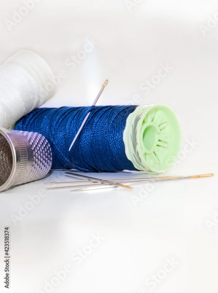 Fototapeta White and blue thread spools with needles and sewing thimble on a brightness white background
