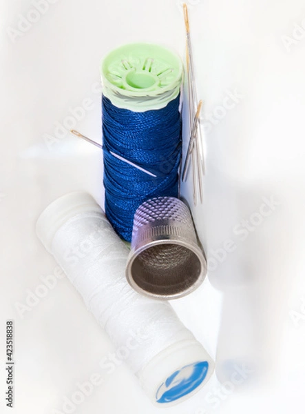 Fototapeta White and blue thread spools with needles and sewing thimble on a brightness white background