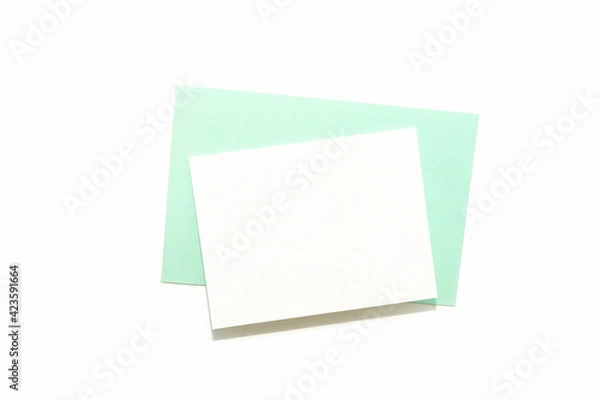 Fototapeta Blank white card on pastel green envelope. Simple minimalist composition on white background. Top view, empty space for text.	