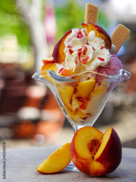 Fototapeta Decorated peach sundae with ice cream, whipped cream and fruits. For ice cream parlors, restaurant and cafe. copy space