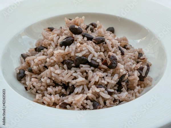 Fototapeta Rice with black beans served in a white bowl on a white tablecloth, widely consumed in the Dominican Republic and known as moro.