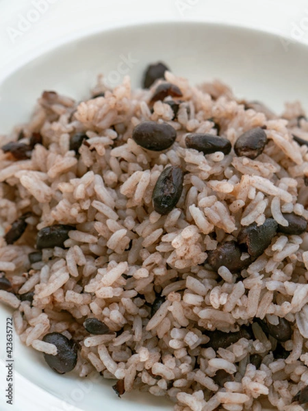 Fototapeta Rice with black beans served in a white bowl on a white tablecloth, widely consumed in the Dominican Republic and known as moro.