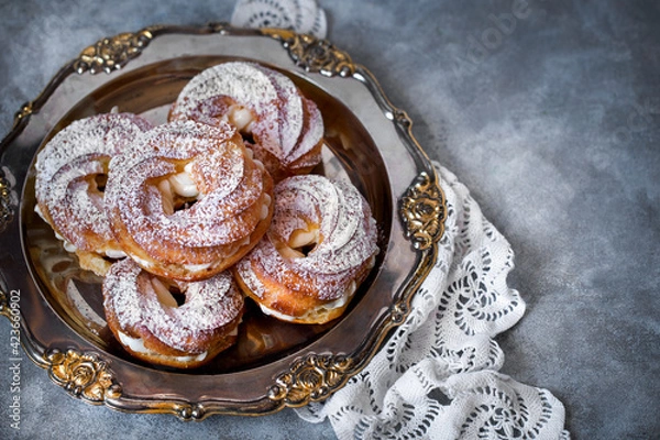 Fototapeta custard cake rings with cream and powdered sugar on a metal platter