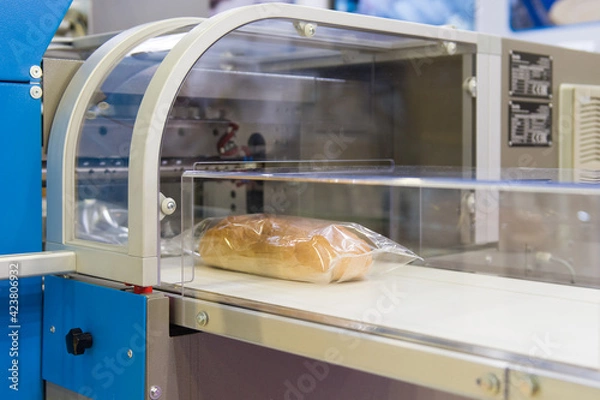 Obraz White bread in plastic packaging on conveyor for packaging 