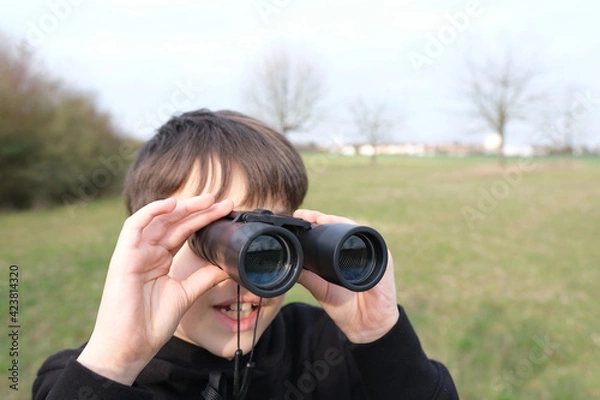 Fototapeta boy, guy 8-10 years old stalker looks through black binoculars in the park, spies, hunts down secrets, the concept of surveillance, observation of people and animals