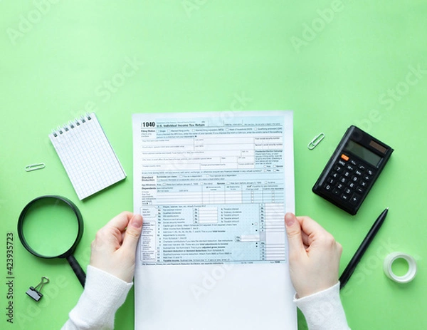 Fototapeta A man holds a 1040 tax form in his hands. Filling out taxation documents. Green background with copy space