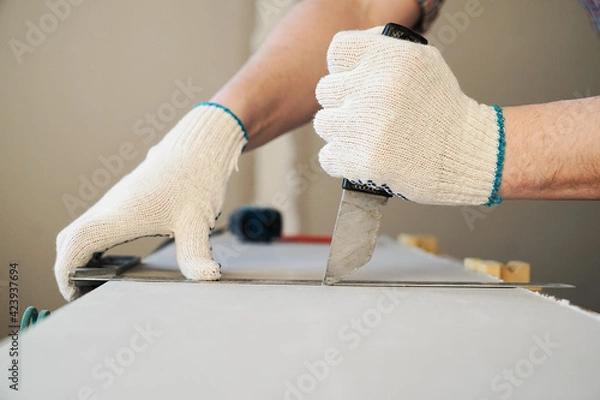 Obraz A man cuts a drywall sheet with a knife