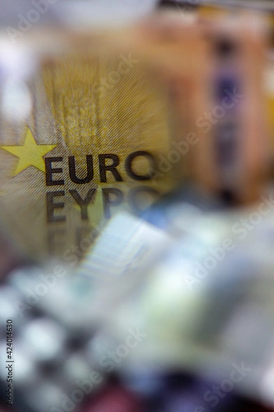 Obraz Word "Euro" on a bill seen through a magnifying glass with a defocused calculator