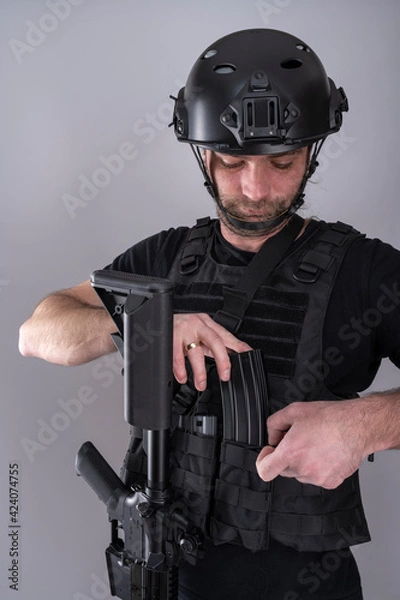 Obraz Close up of male equipped for airsoft adding an extra magazine to his vest while looking down.