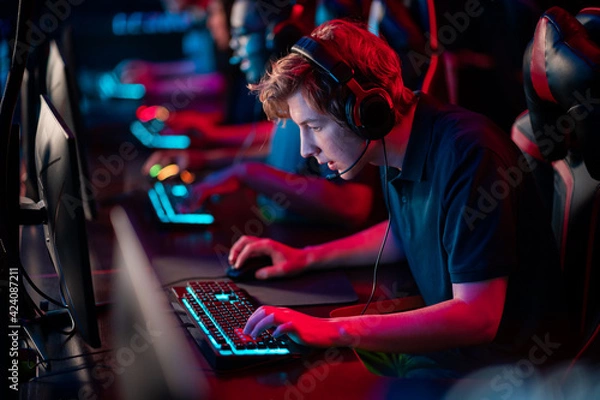 Fototapeta A multi-racial team of esports athletes conducts a training session before an online shooter tournament. Neon light.