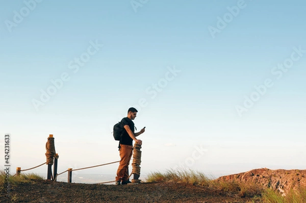 Fototapeta Latin man using smart phone after a hiking trail in the mountains