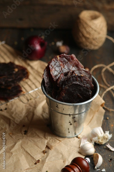 Fototapeta Homemade beef jerky seasoned with garlic, onion, pepper and salt. Jerky in a bucket on a wooden background
