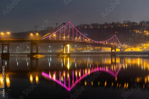 Fototapeta Pedestrian bridge in Kiev. Evening lighting. Reflection of the bridge in the river.