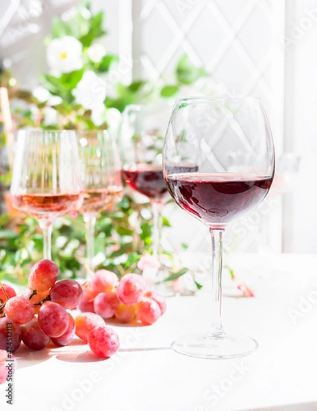 Fototapeta Red wine in a glass on a light concrete background in the rays of the sun.