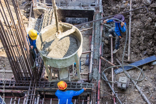 Obraz Worker pouring cement pouring into foundations formwork at building area in construction site.
