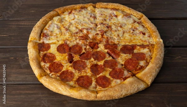 Fototapeta delicious pizza on a wooden background. Peperoni and Hawaiian, combined pizza in two parts. traditional Italian dish in the form of a thin round tortilla made of yeast dough and stuffed. fast food.