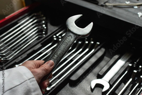 Obraz Hand of a caucasian man holding a wrench with a set of wrenches in the background