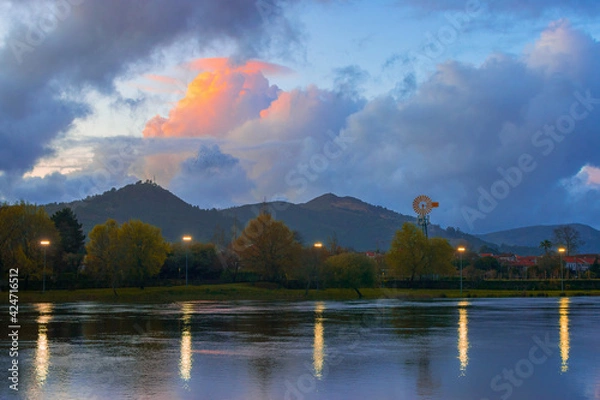 Obraz Scenic landscape view of a river with a windmill next to the mountains during the blue hour in the dawn, Limia River, Ponte de Lima, Portugal
