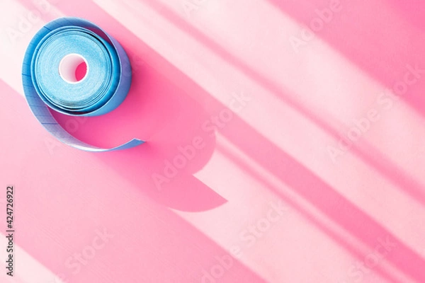 Obraz Blue roll of kinesiology tape on pink background with trendy sun light and shadows and copy space, flat lay. Recovery, anti-aging procedures. Kinesio taping
