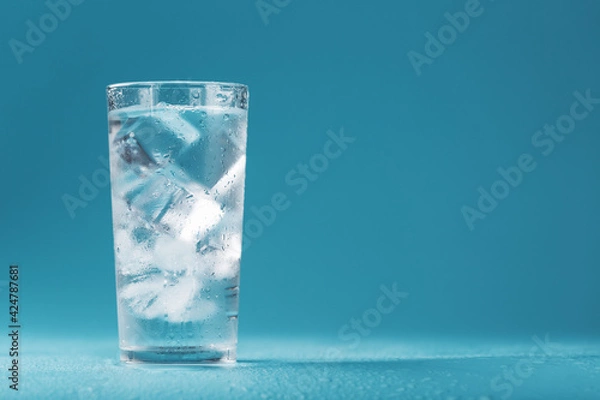 Fototapeta Ice cubes in a glass with crystal clear water on a blue background.