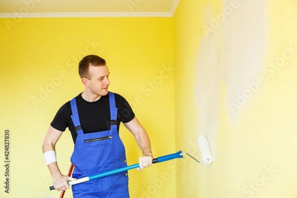 Fototapeta A young man makes repairs to the apartment, ok re-paints the walls in a different color