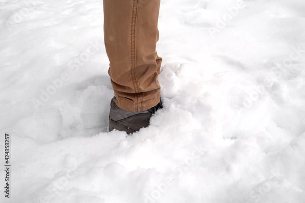 Fototapeta Man legs standing in fresh snow. Footprints of shoes in the snow. Snowdrifts in the winter