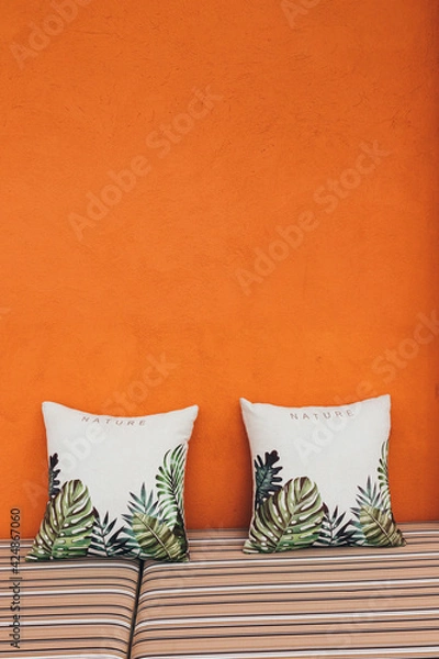Obraz Two pillows against the background of an orange textured wall with a striped sofa in a modern cafe