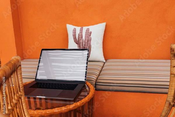 Obraz A laptop on a glass table, a pillow against the background of an orange textured wall in a modern cafe. Copy space