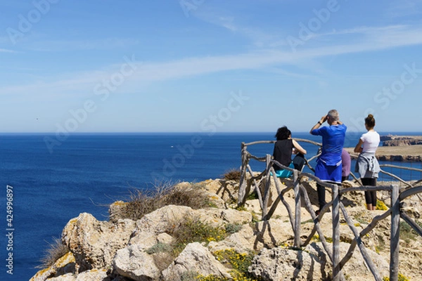 Fototapeta Group of hikers observing Punta Nati Lighthouse from the Sa Falconera point of view, in Menorca (Balearic Islands, Spain)