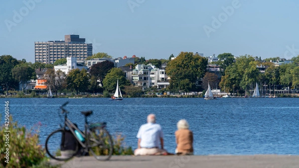 Obraz hamburg alster lakeview on a sunny day with to people in the front sitting near by the water with a parking bike, germany