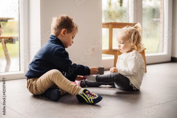 Obraz Grand frère aide sa petite sœur à mettre ses chaussures. Un beau moment de complicité entre ces deux petits enfants 