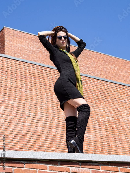 Obraz Mujer delgada vestida de negro, posando con gafas de sol y botas altas, primavera 2021.