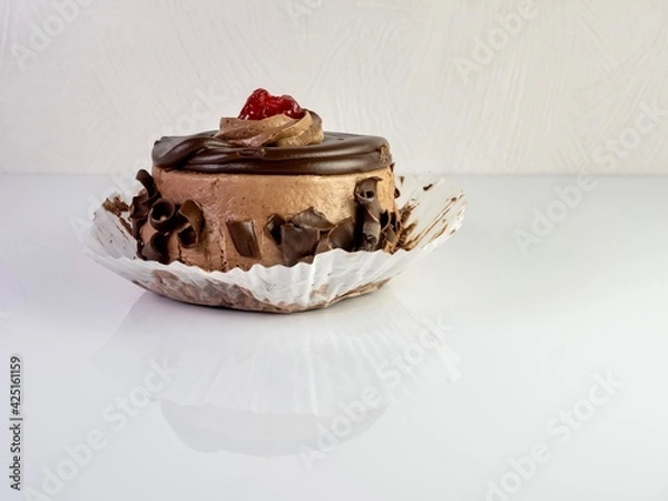 Obraz Chocolate mini cake with chocolate frosting, curled chocolate and a berry on top, sitting on a white counter with the reflection showing, a delicious indulgence of a sweet dessert waiting to be eaten.