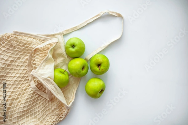 Fototapeta Zero waste shopping concept. Fresh vegetables in eco cotton bags on table in the kitchen. View from above on eco friendly bag filled with green organic apples, zero waste informed consumption concept