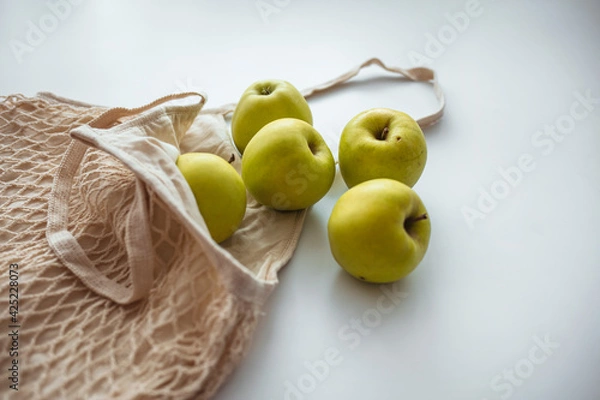 Fototapeta Zero waste shopping concept. Fresh vegetables in eco cotton bags on table in the kitchen. View from above on eco friendly bag filled with green organic apples, zero waste informed consumption concept