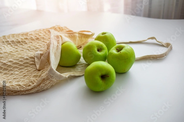 Fototapeta Zero waste shopping concept. Fresh vegetables in eco cotton bags on table in the kitchen. Apples in sustainable and ecological shopping bag. Zero waste consumption concept