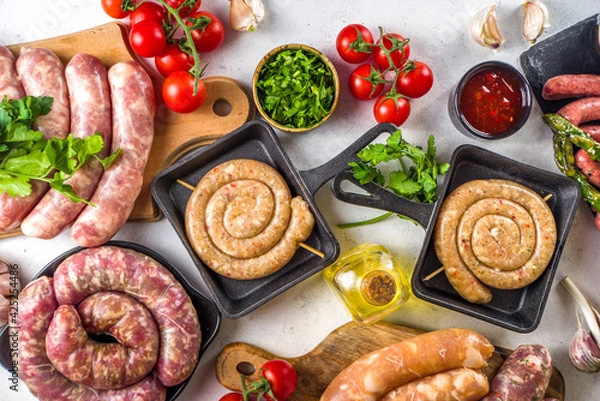 Fototapeta Set of different raw beef, pork and chicken meat sausages on cooking table with spices, sauces and vegetables for grilling. Bbq party concept, white background top view copy space