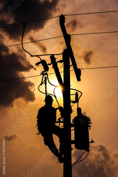 Fototapeta The silhouette of power lineman climbing on an electric pole with a transformer installed. And replacing the damaged hotline clamp, bail clamp, dropout and surge arrester that causes a power failure.