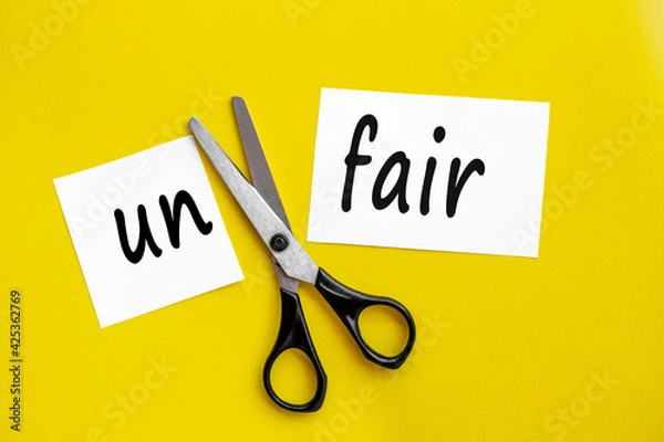 Fototapeta Cutting Unfair to Fair Paper Sign with Scissors on a yellow background. Woman doing justice to herself by cutting the word, changing into fair