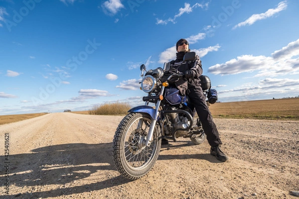 Fototapeta  man in a black uniform on bike against the backdrop of panorama of field and blue sky. motorcycle travel concept