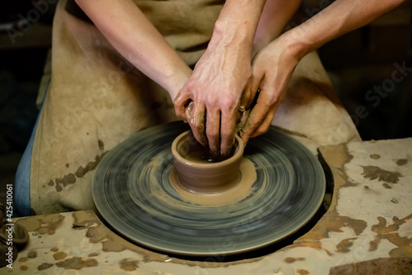 Fototapeta Pottery classes, student making clay pot on wheel. Close-up of dirty hands, sculpting clay crockery pottery training