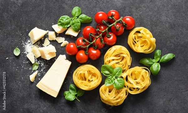Fototapeta Tagliatele pasta, tomatoes, basil and parmesan cheese on a black concrete background. Ingredients for pasta with text space. Layout.