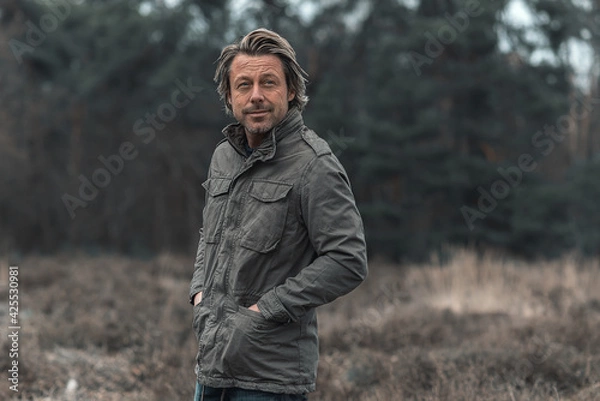 Fototapeta Smiling blond man in green coat on heathland in nature reserve.